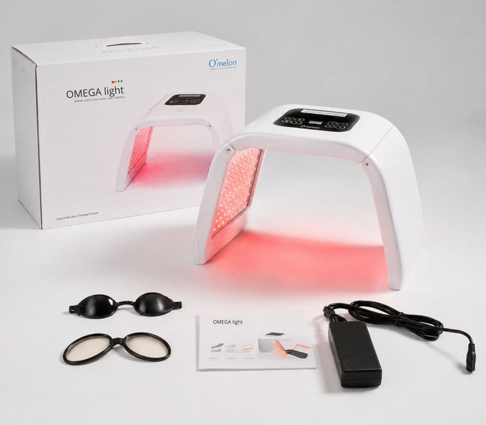 Omega Light device with packaging, goggles, and power adapter on a beige background