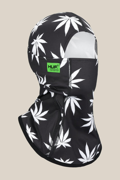 A black 686 Alpha Hinged Balaclava with white marijuana leaf prints and a green 686 logo patch on the side, shown on a plain light beige background.
