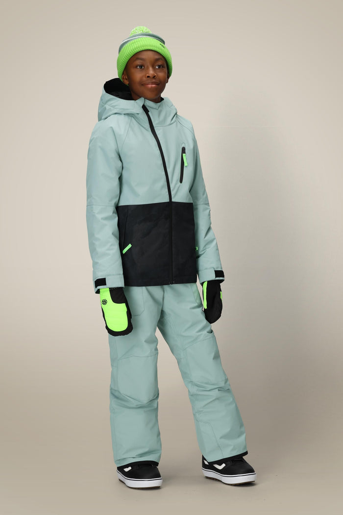 A smiling child in the 686 Boys' Hydra™ Insulated Jacket by 686, paired with winter pants, a neon green beanie, and matching gloves, stands indoors against a plain beige background.