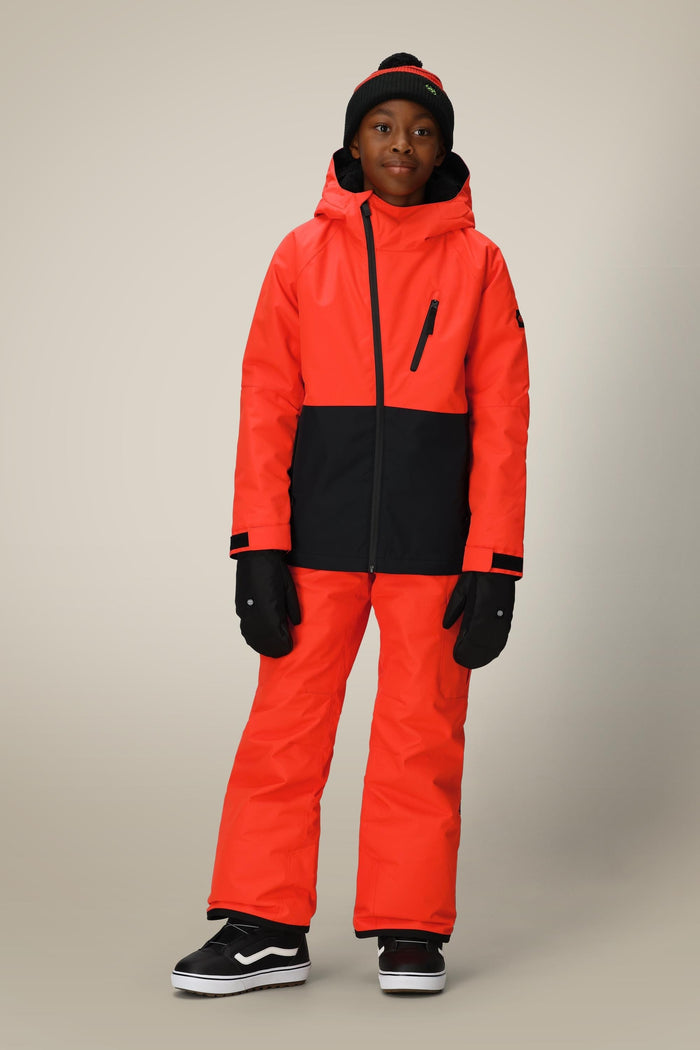 A young boy poses against a plain light background wearing the 686 Boys' Hydra™ Insulated Jacket in bright orange and black, paired with black gloves, a black and red beanie, and black sneakers.