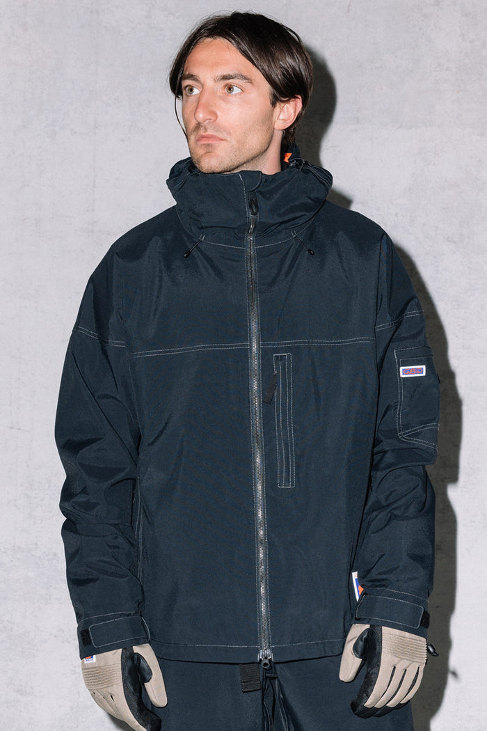 A man with short brown hair wears the 686 Dojo® Jacket by 686, along with taupe gloves and dark pants, standing against a light gray background.