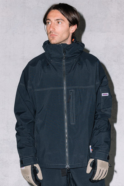 A man with short brown hair wears the 686 Dojo® Jacket by 686, along with taupe gloves and dark pants, standing against a light gray background.