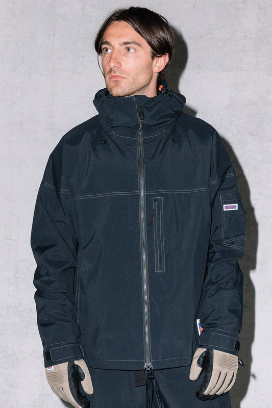 A man with short brown hair wears the 686 Dojo® Jacket by 686, along with taupe gloves and dark pants, standing against a light gray background.