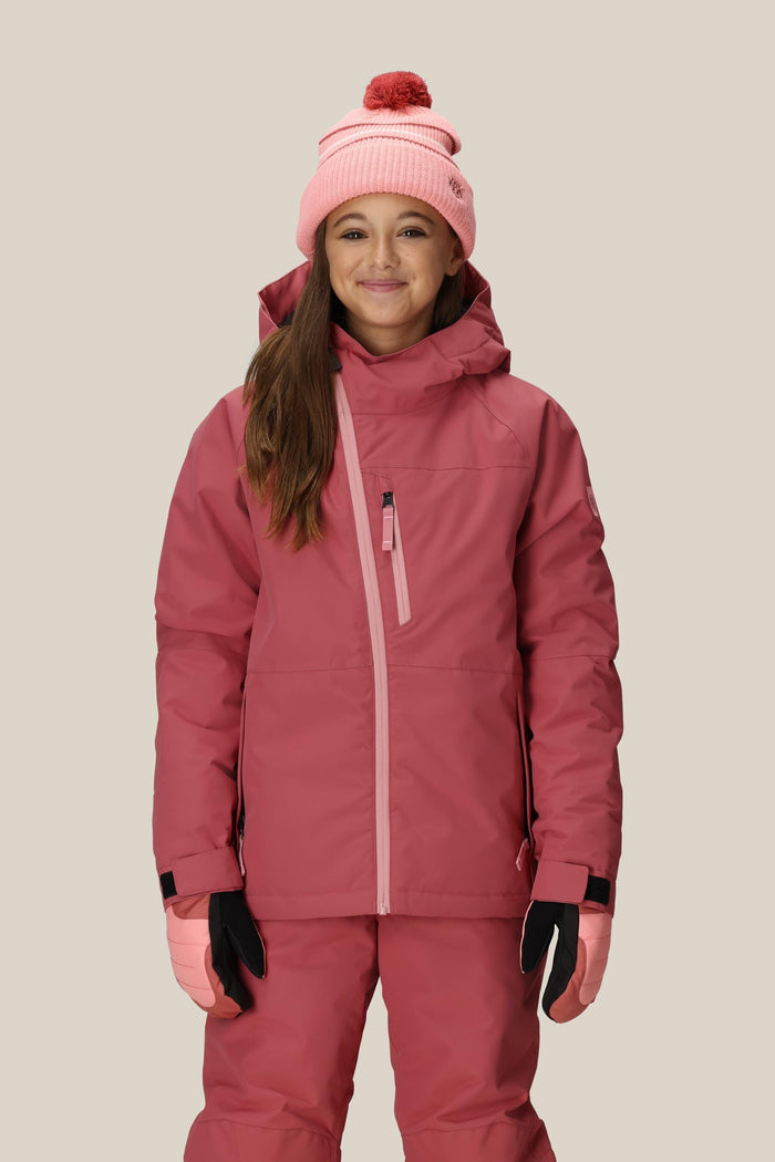 A smiling girl wears the 686 Girls' Hydra™ Insulated Jacket by 686, matching pink pants, a pink knit pom-pom hat, pink gloves, and black glove liners, standing against a plain light background.
