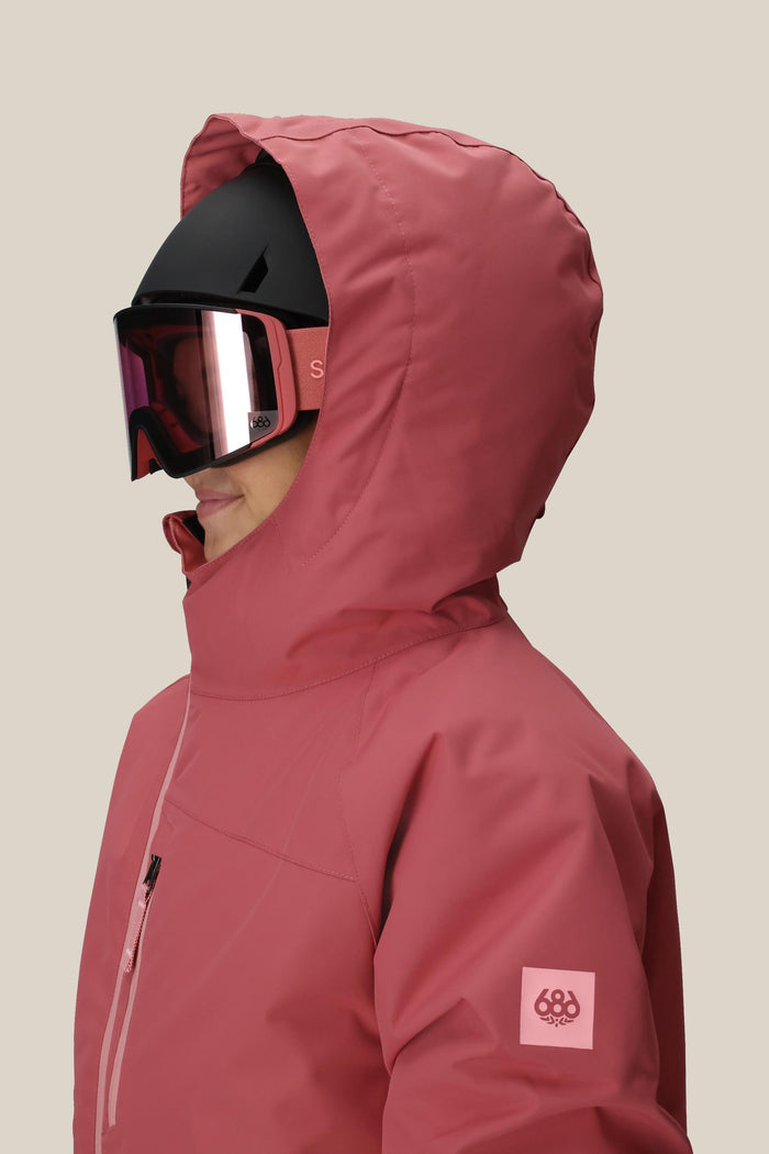 A girl wears the 686 Girls' Hydra™ Insulated Jacket in rose, paired with a black ski helmet and pink-tinted goggles, shown in profile against a plain beige background.