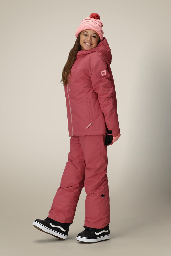 A smiling girl poses in the 686 Girls' Hydra™ Insulated Jacket, paired with matching pants and a beanie. She stands against a plain background, wearing black snow boots, looking cheerful and ready for winter fun.