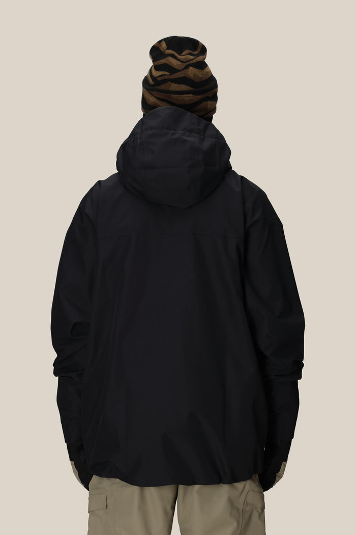 A person is shown from the back against a plain, light background wearing a 686 Mens Gateway Shell Jacket in black, beige pants, and a brown and black striped beanie.
