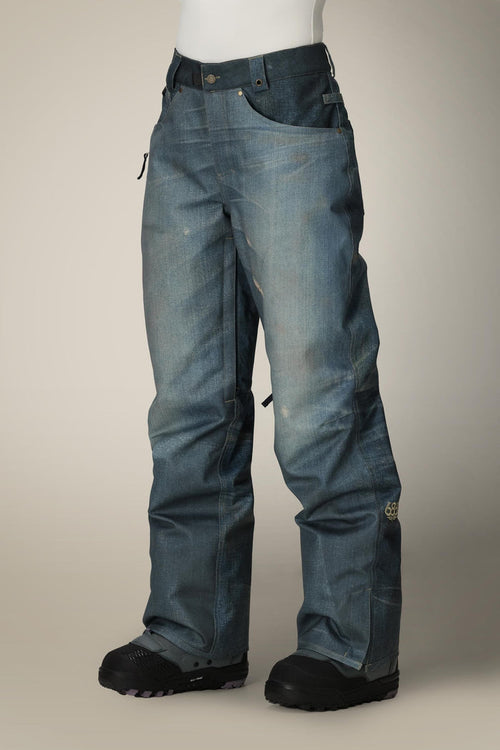 A mannequin wears 686 Women's Deconstructed™ Denim Insulated Pant by 686—loose-fit, blue, denim-look waterproof pants with button closure, belt loops, visible seams—paired with black snow boots.