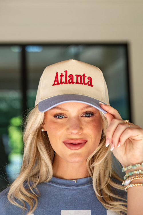 Woman wearing a beige cap with 'Atlanta' embroidered on it, indoors.