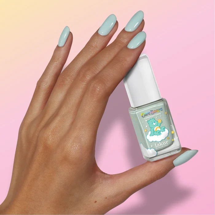 A hand with light blue painted nails holds a matching bottle of LONDONTOWN’s Beary Minty nail polish against a pink gradient background, creating an airy sense of hopeful clarity.