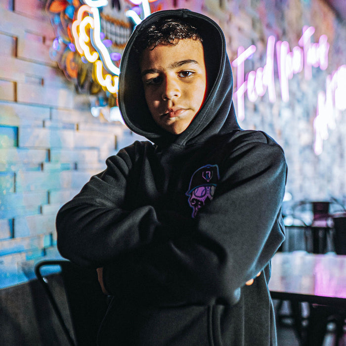 Person wearing a black hoodie with a blue and white skull graphic in front of neon signs