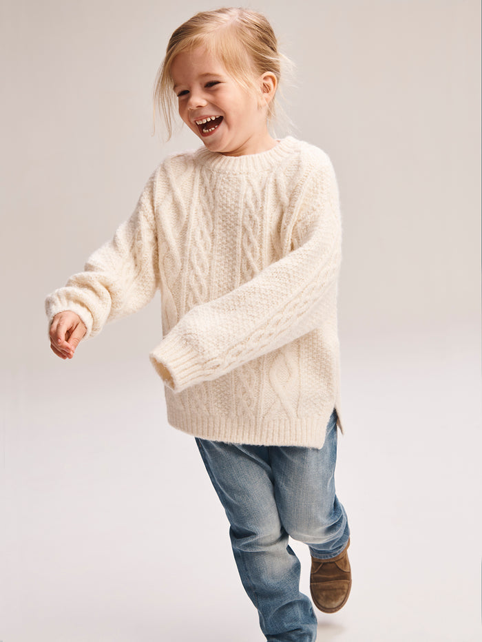 DL1961 boys' Brady Slim jeans in light blue 'Fresh', worn by a laughing child in a cream cable-knit sweater, mid-stride.