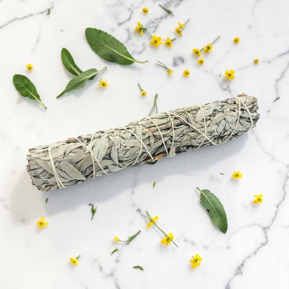 Sage bundle on a marble surface with scattered leaves and flowers