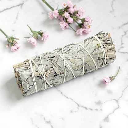 Rolled sage bundle tied with twine on a marble surface with small pink flowers.