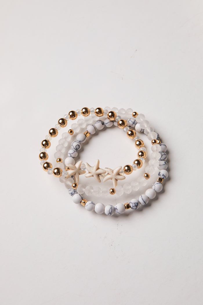 Set of three beaded bracelets with gold beads and starfish charm on a light background