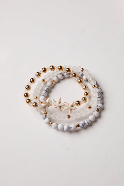 Set of three beaded bracelets with gold beads and starfish charm on a light background