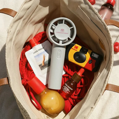 An open tote bag contains the LONDONTOWN Cool Set Nail Fan - Cloud to help with dry times, a disposable camera, red rope, lotion pouch, two bottles with droppers, and a yellow spray bottle.
