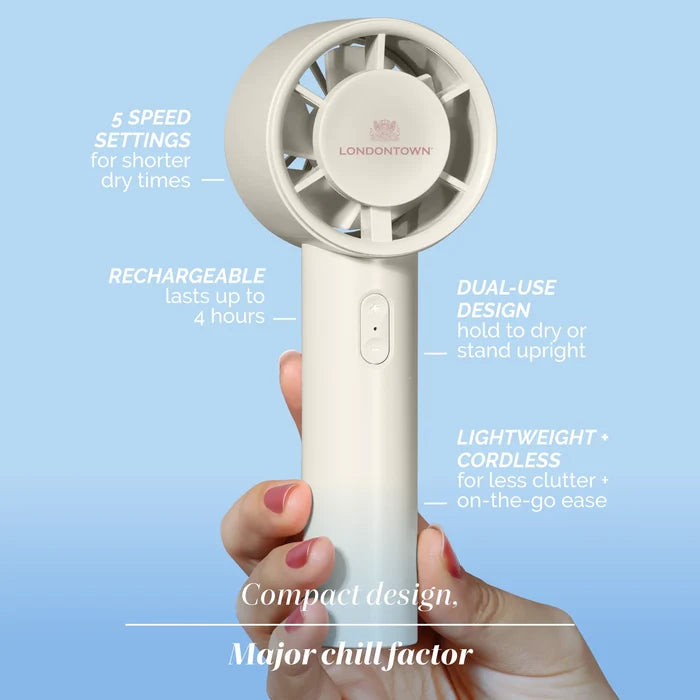 A hand holds the LONDONTOWN Cool Set Nail Fan - Cloud, a white handheld fan with labeled features such as five speeds, rechargeable power, a dual-use design, and cordless operation against a blue background—perfect for reducing dry times wherever you go.