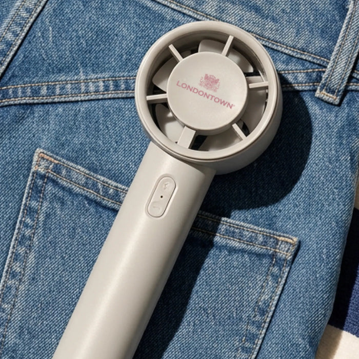 A Cool Set Nail Fan - Cloud by LONDONTOWN rests on blue denim fabric with visible pocket stitching in natural light, highlighting it as the perfect accessory for speedy nail drying.