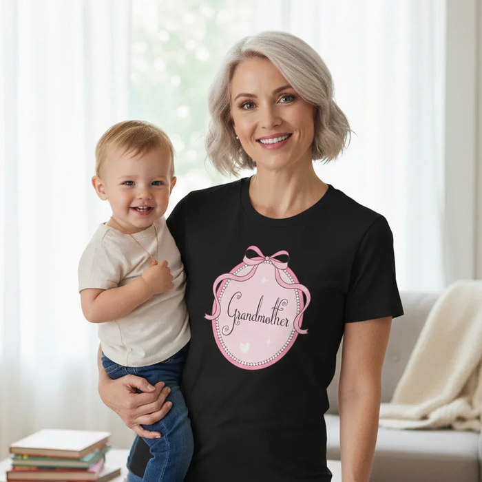 Woman wearing a black t-shirt with 'Grandmother' design, holding a child in a living room.