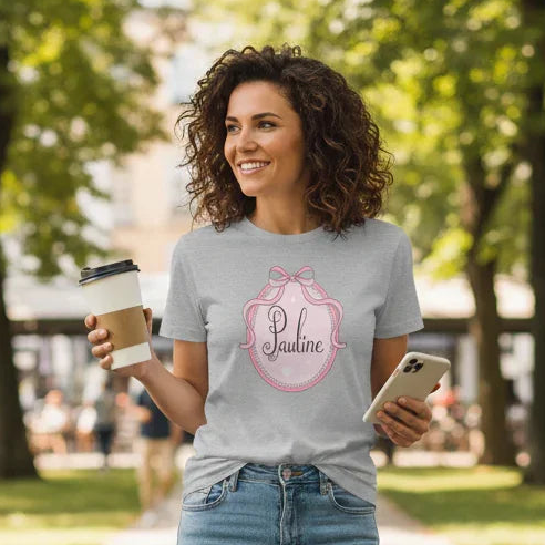 Woman walking in a park holding a coffee cup and phone, wearing a branded t-shirt.