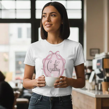 Woman holding a coffee cup in a cafe wearing a white t-shirt with a pink design.