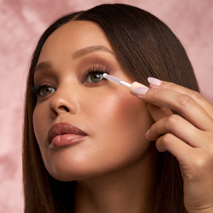 Close-up of a woman applying makeup remover to the eye with a wand against a pink backdrop