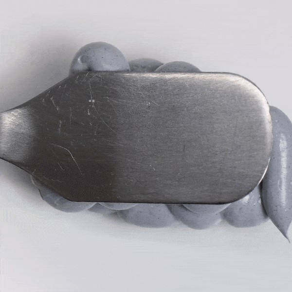 Detox Activated Charcoal Mask being spread with a metal spatula on a clean surface.