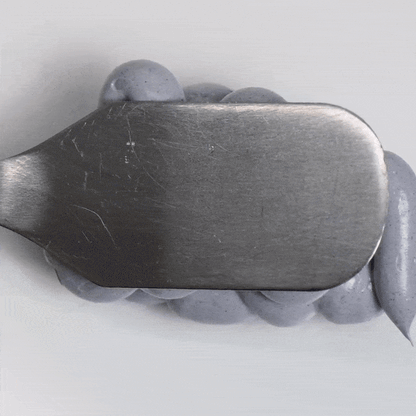 Detox Activated Charcoal Mask being spread with a metal spatula on a clean surface.