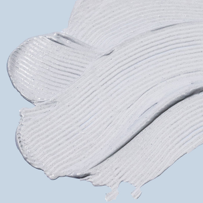 Close-up of a light gray charcoal facial mask smeared across a pale blue background