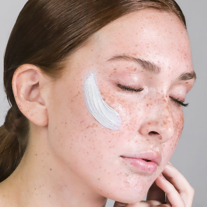Side profile of a woman with a white facial mask applied along her cheek and jawline