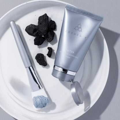 CosMedix Detox charcoal mask tube with a spatula and chunks of charcoal on a white plate