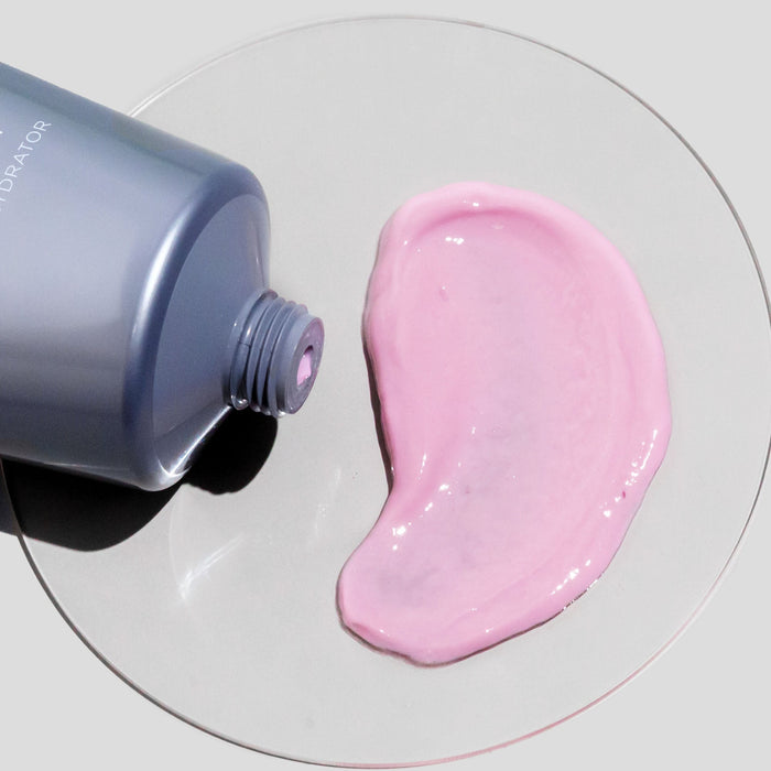 Emulsion Intense Hydrator tube laying flat on light gray surface with glass petri dish with pink product