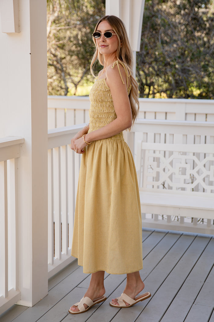 Woman in a yellow dress standing on a wooden deck with white railings.