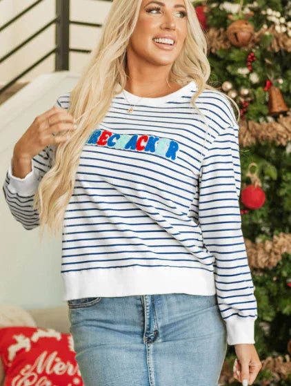 Smiling woman with long blonde hair wearing striped sweater and light denim skirt near Christmas tree and red holiday pillow