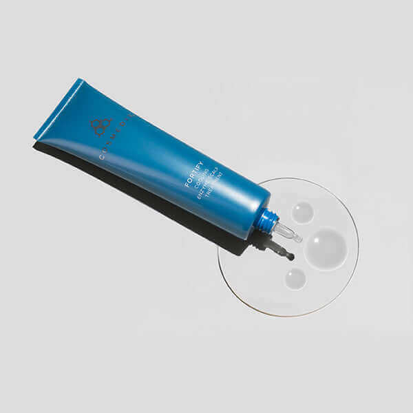 Blue Fortify Cooling Enzyme Scalp Treatment tube angled on a white background with a glass plate and droplets.