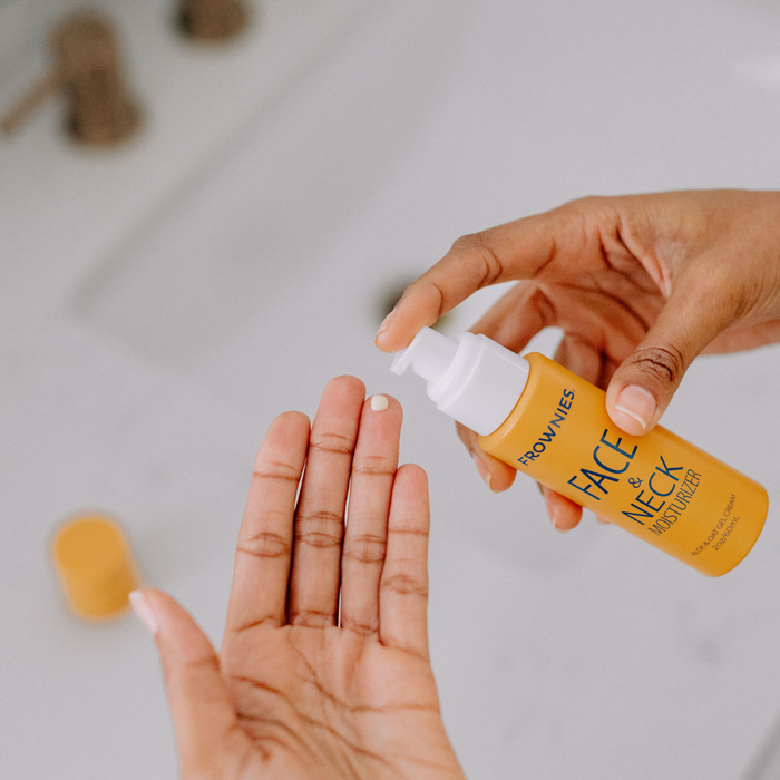 Person applying Frownies Face & Neck Moisturizer to their hand on a neutral background