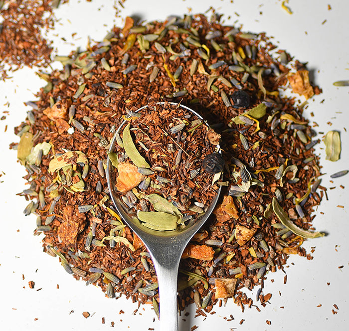 Lake Missoula Tea Company's Gin & Cream herbal tea in a teacup with a tea bag and fresh herbs on a wooden table.