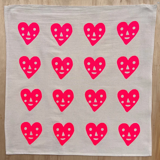 Light gray tea towel with repeating pink heart faces pattern