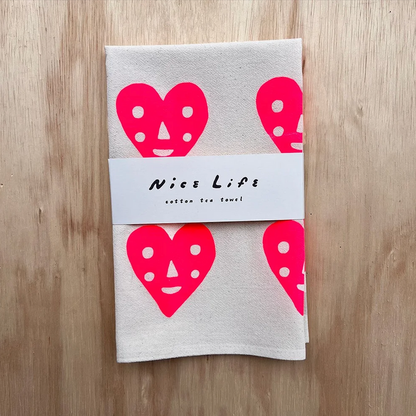 Folded light gray tea towel with pink heart faces and 'Nice Life' label