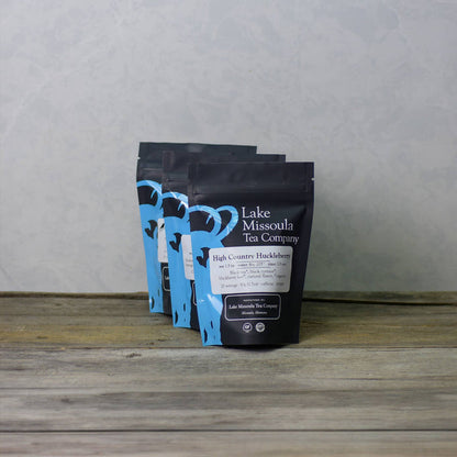 Lake Missoula Tea Company's High Country Huckleberry tea in a clear glass cup with fresh huckleberries and tea leaves.