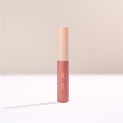 HOL bonding glue tube standing upright with pale pink cap against a soft beige backdrop