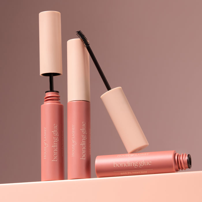 Mascara wand lifted from a pink tube, the brush near the cap against a warm brown background