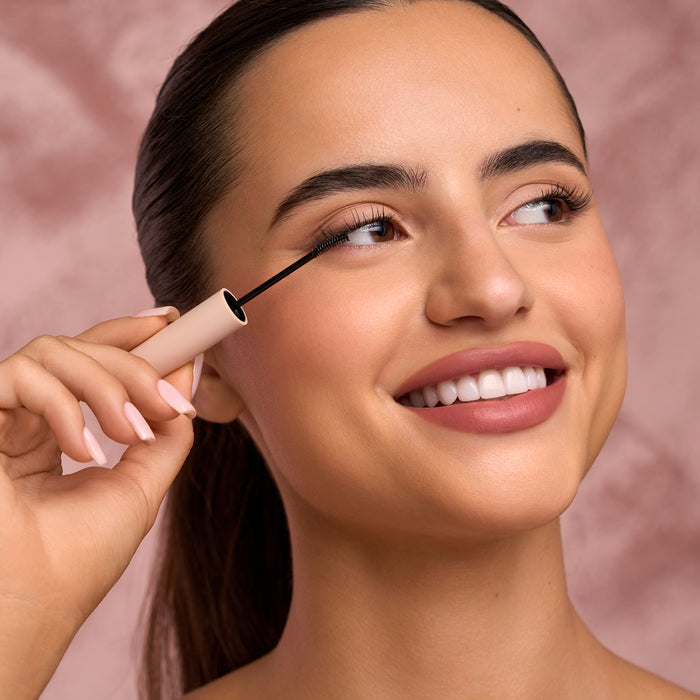Close up of a model applying mascara to her lashes with a wand near the eye and brow