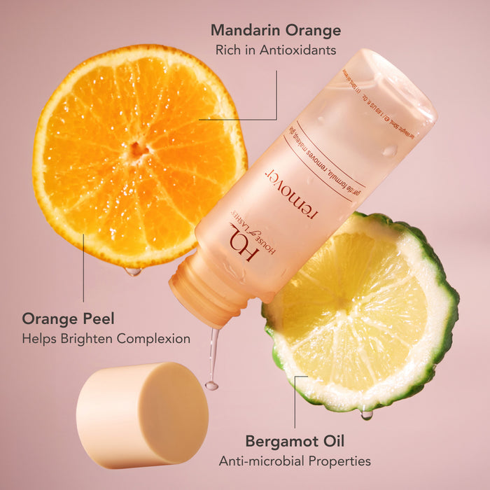 Mandarin orange half and bergamot oil highlights beside a tilted HOL Lash Glue Eye Makeup Remover bottle.
