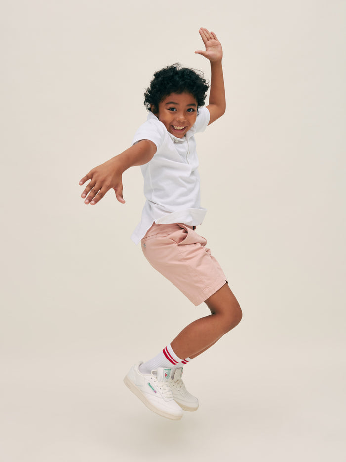 DL1961 boys' Jacob Short in dusty pink 'Rose Smoke' worn by boy jumping in white polo, side view.