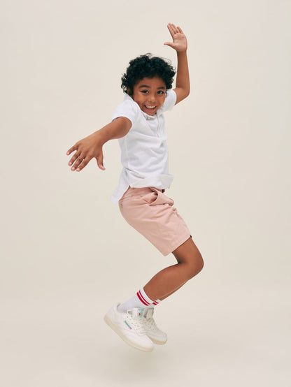 DL1961 boys' Jacob Short in dusty pink 'Rose Smoke' worn by boy jumping in white polo, side view.