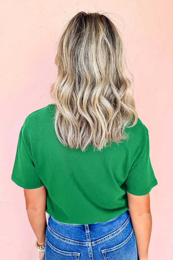 Back view of woman with wavy blonde hair wearing green shirt and blue jeans against pink wall
