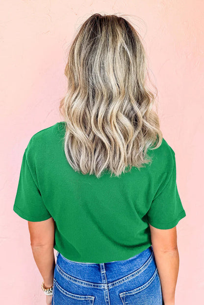 Back view of woman with wavy blonde hair wearing green shirt and blue jeans against pink wall