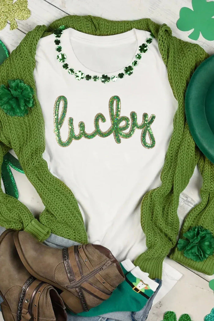 Baby onesie with 'lucky' text and green shamrock design, wrapped in a green blanket with shamrock patterns.